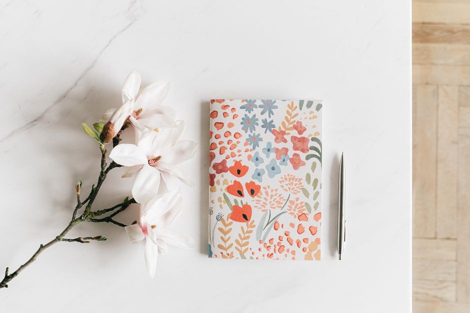 Floral-covered notebook beside pale flowers on a light tabletop.